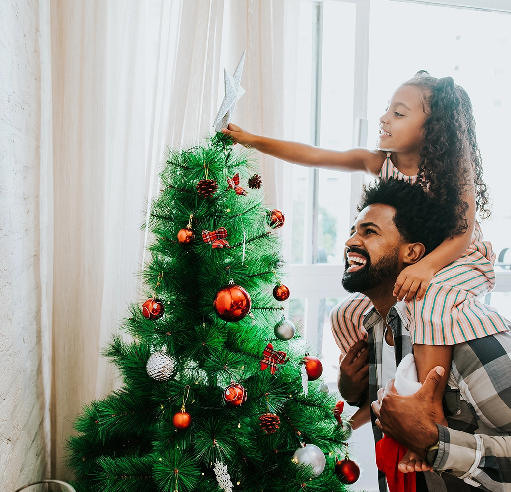 Dad with daughter on his shoulders decorating the Christmas tree