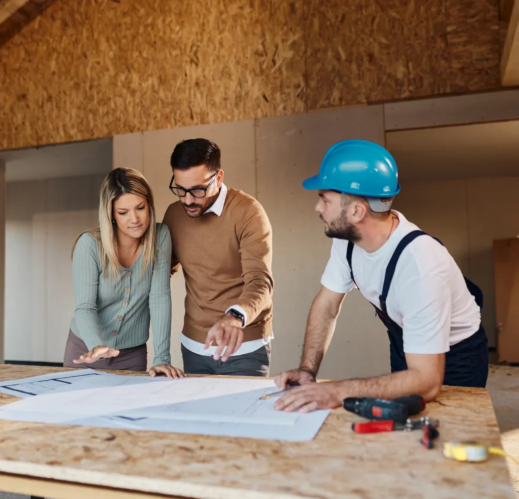 A man in a hard hat shows a blueprint to a man and woman at a construction site