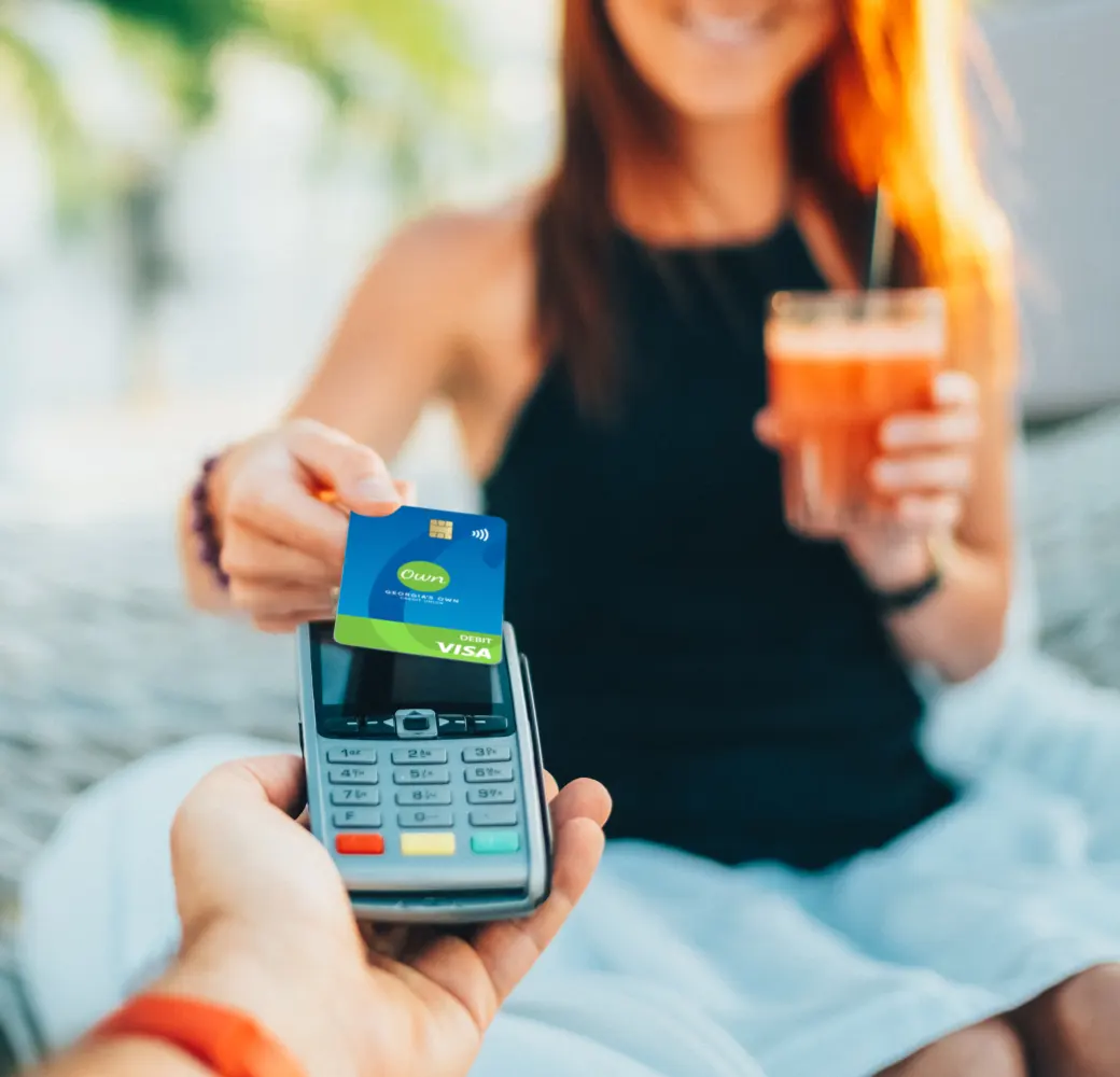 Woman holding a cocktail while using contactless payment wither her debit card