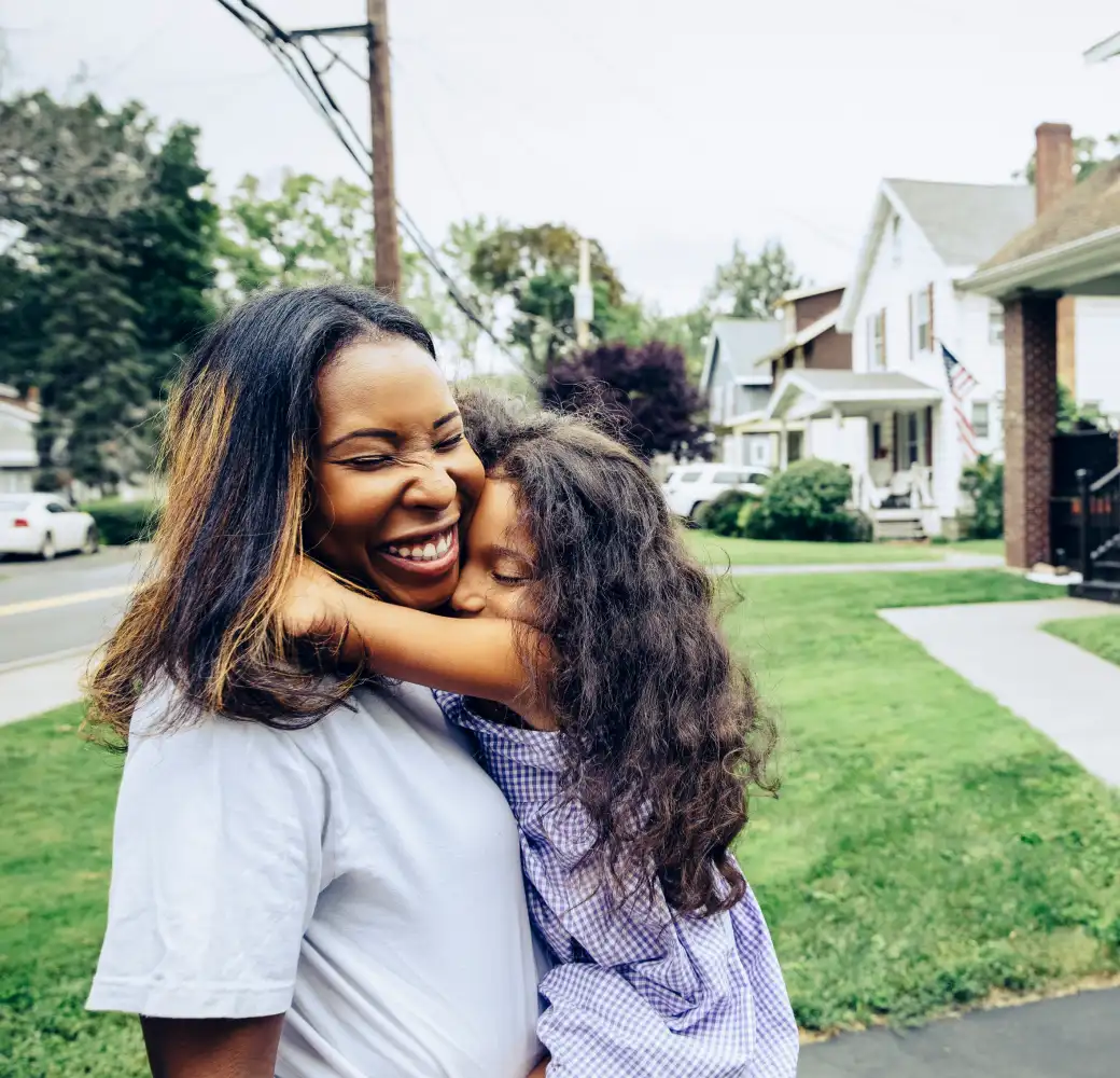 Woman holding a young girl and smiling on her front lawn