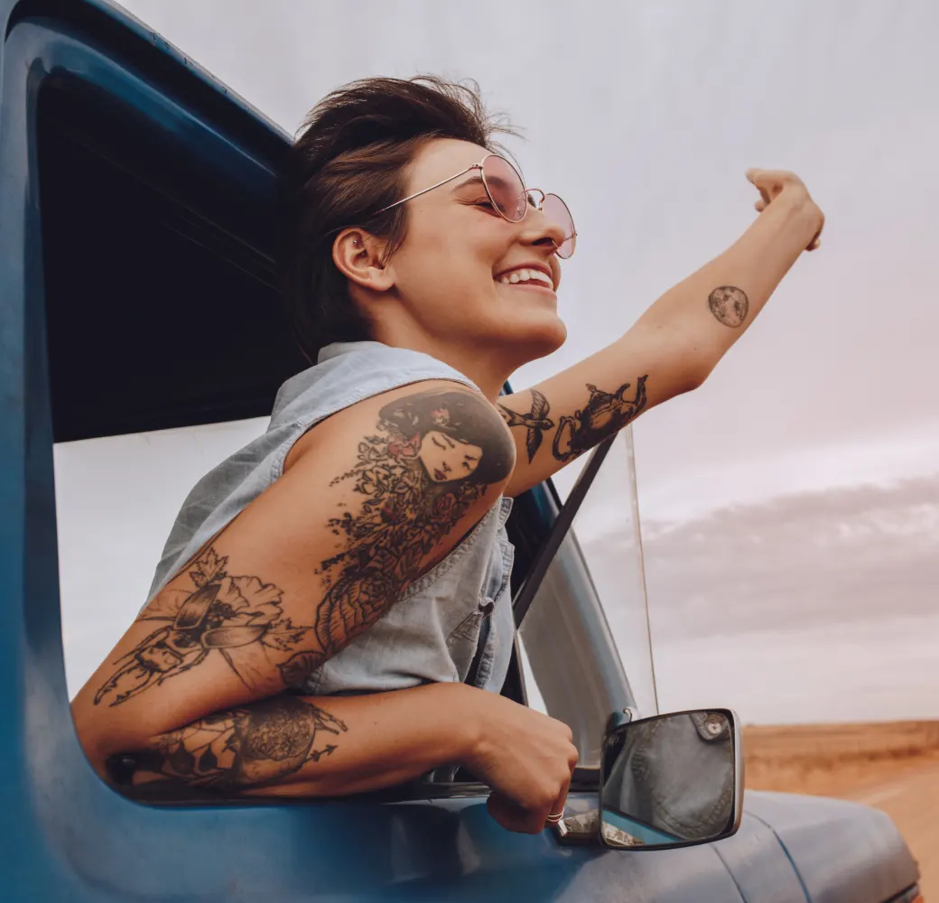 Woman in sunglasses hanging out of car window and waving