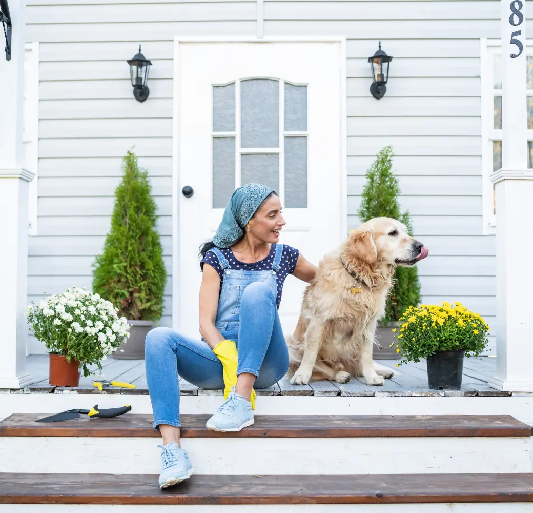 Woman wearing gardening gloves sitting on her front steps with a dog