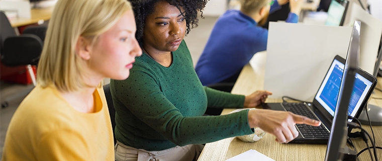 2 women looking and pointing at a computer