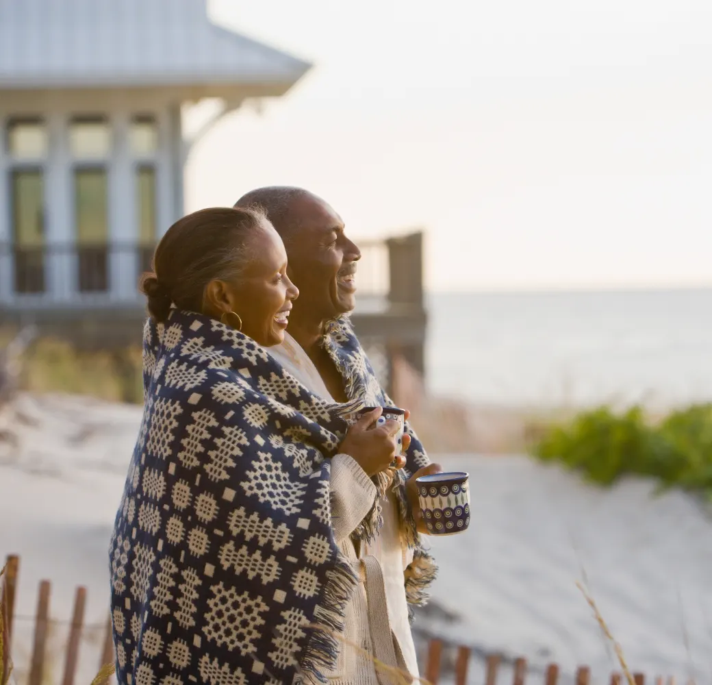 An older couple standing near a beach house watching the sun set