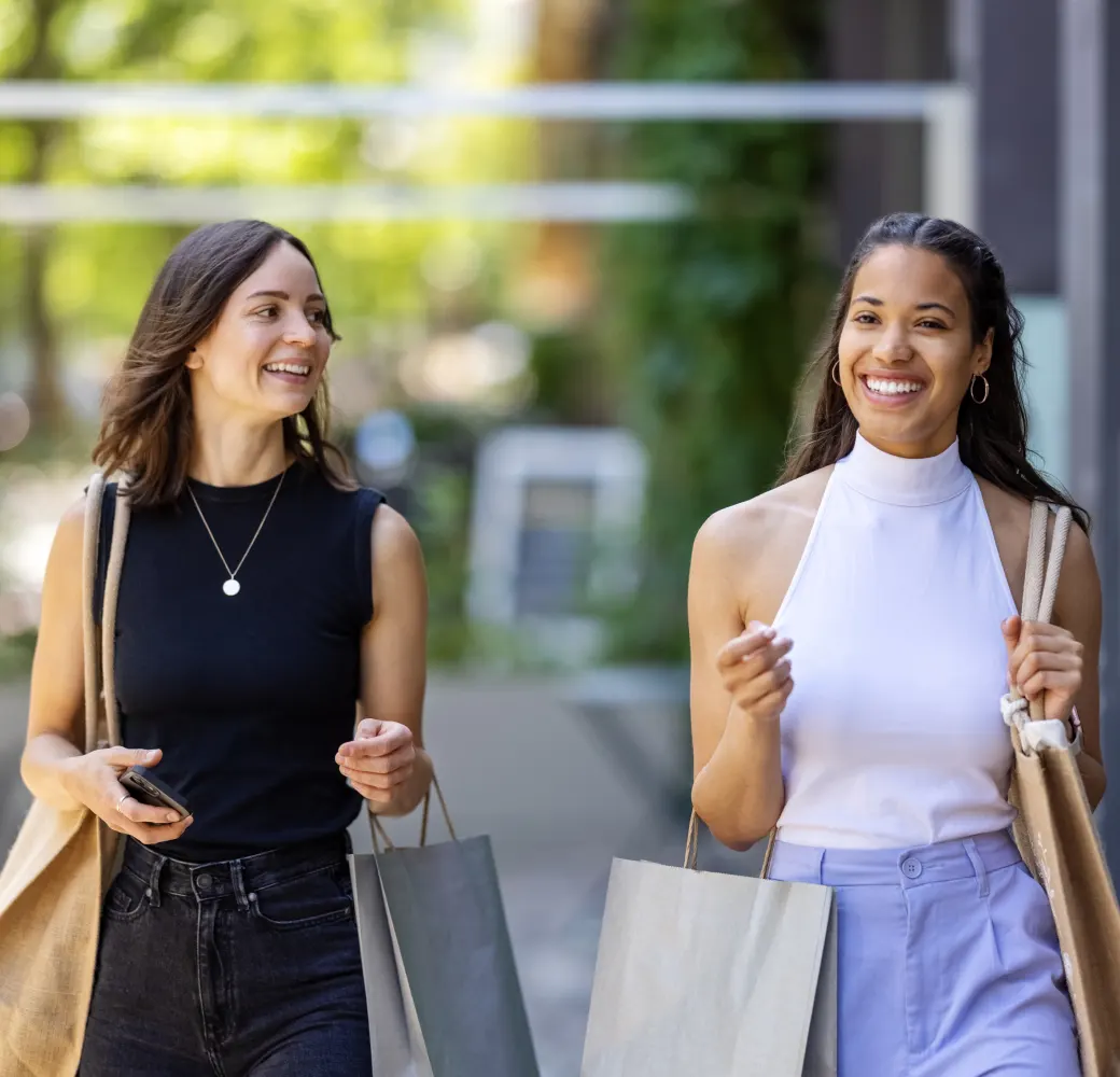 Two women walking down the street together carrying shopping bags and smiling
