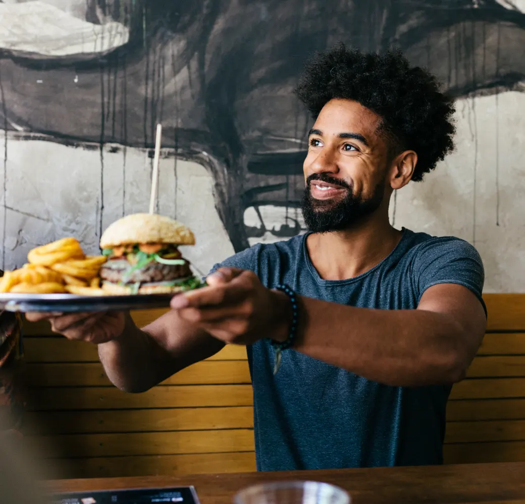 Bearded man handing an order of burgers and fries to someone offscreen