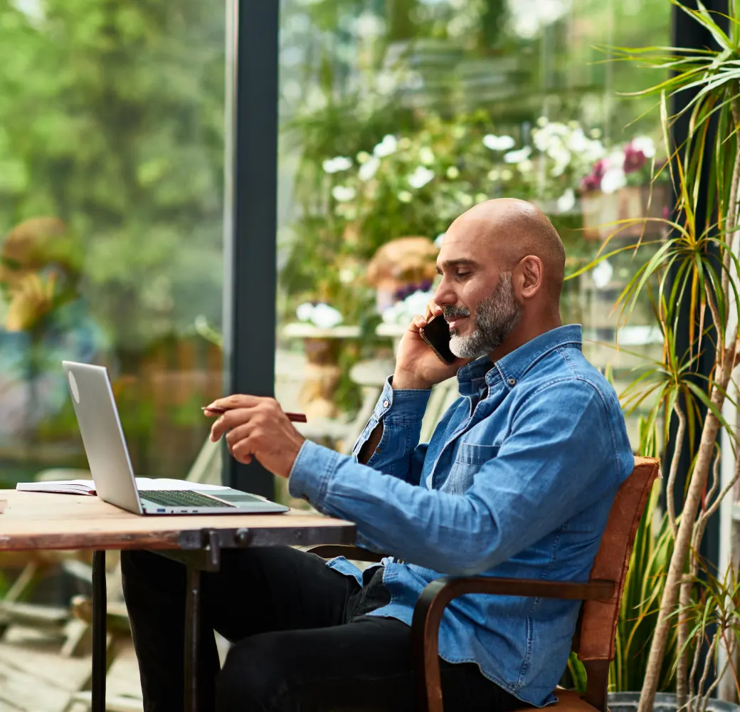 Man sitting in cafe looking at his laptop while taking on his phone