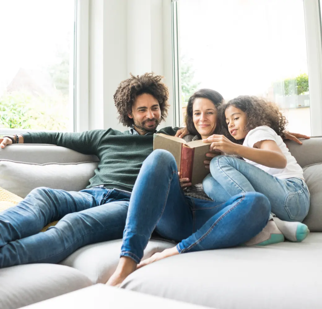A man, woman, and child reading a book together on the couch
