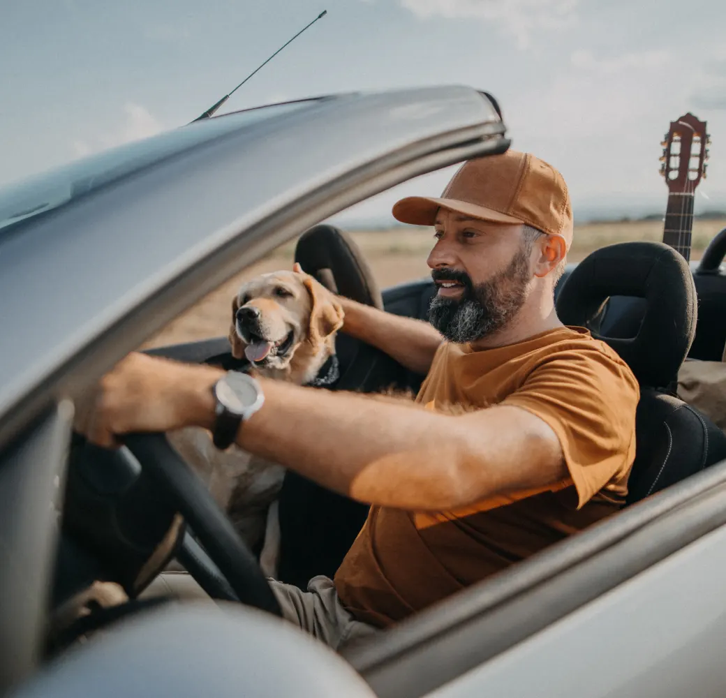 Bearded man driving a convertible with a dog in the passenger seat