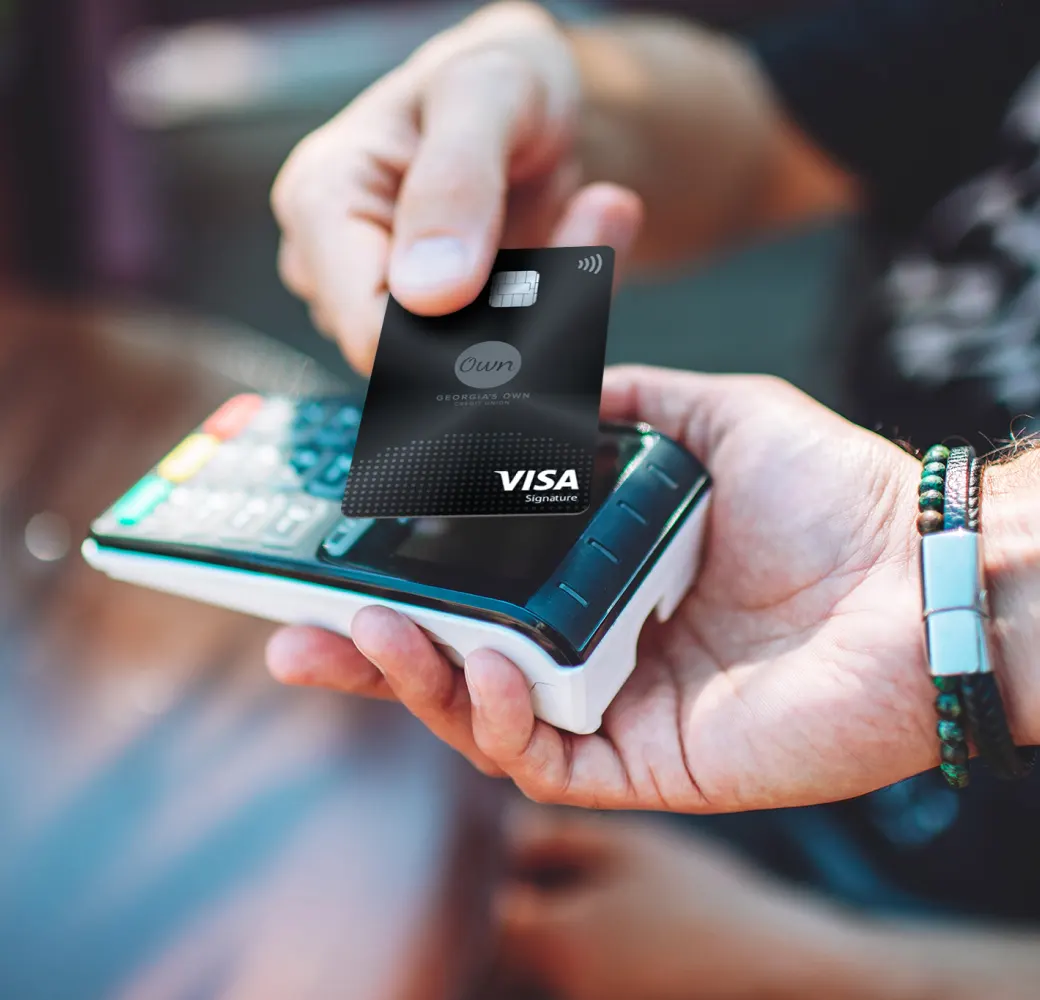 A hand reaching out to hold a Visa credit card over a card reader