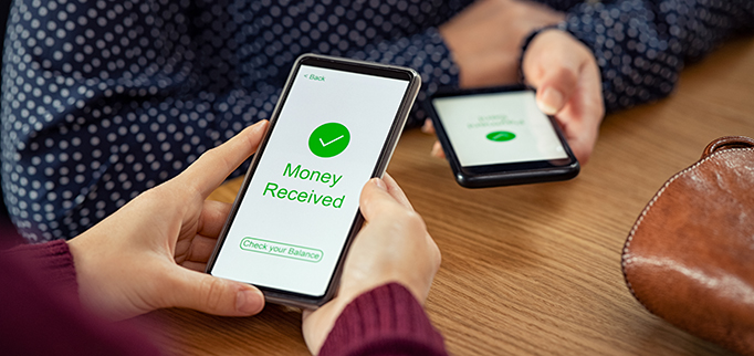 Close up of woman hands holding mobile phone with application to receive money. People holding smart phone and making cashless payment transaction in a shop. Close up of smartphone screen displaying payment sent with money received message.