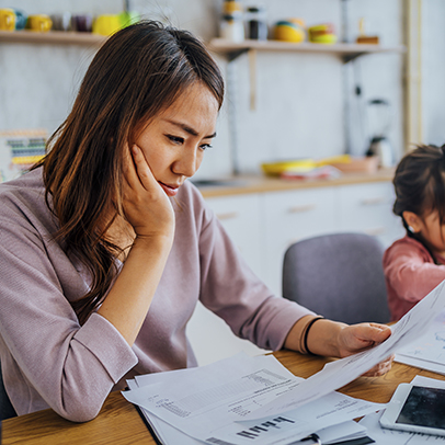 Young stressed mother checking her finances while her daughter is playing next to her