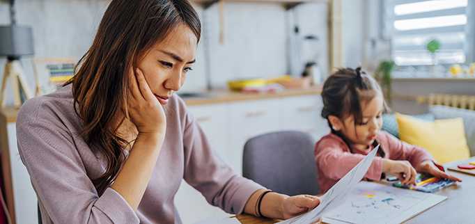 Young stressed mother checking her finances while her daughter is playing next to her