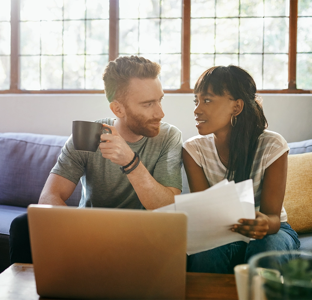 Couple sitting on couch having coffee and looking at paperwork