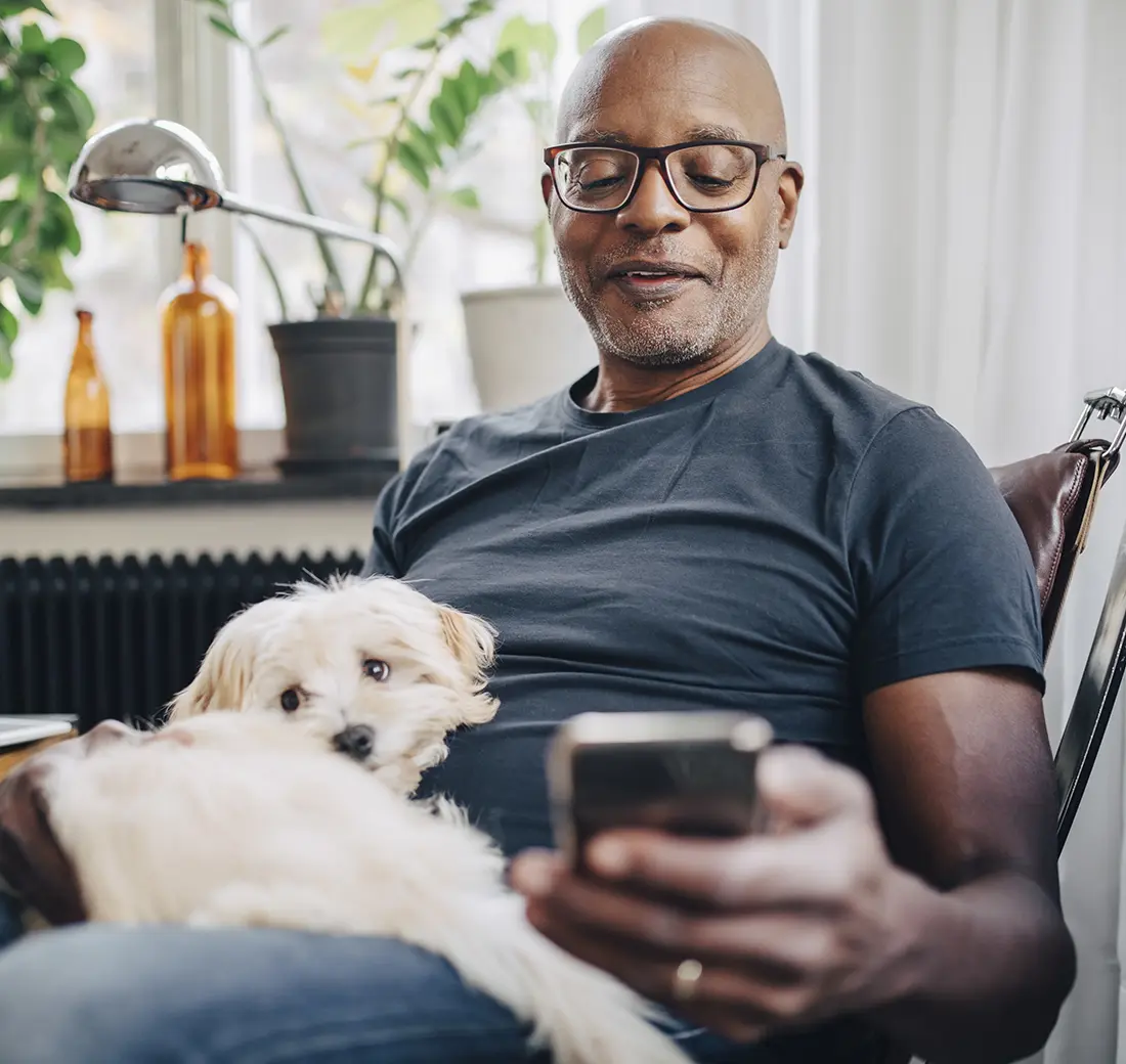 Older black man on the couch looking at phone with dog in his lap