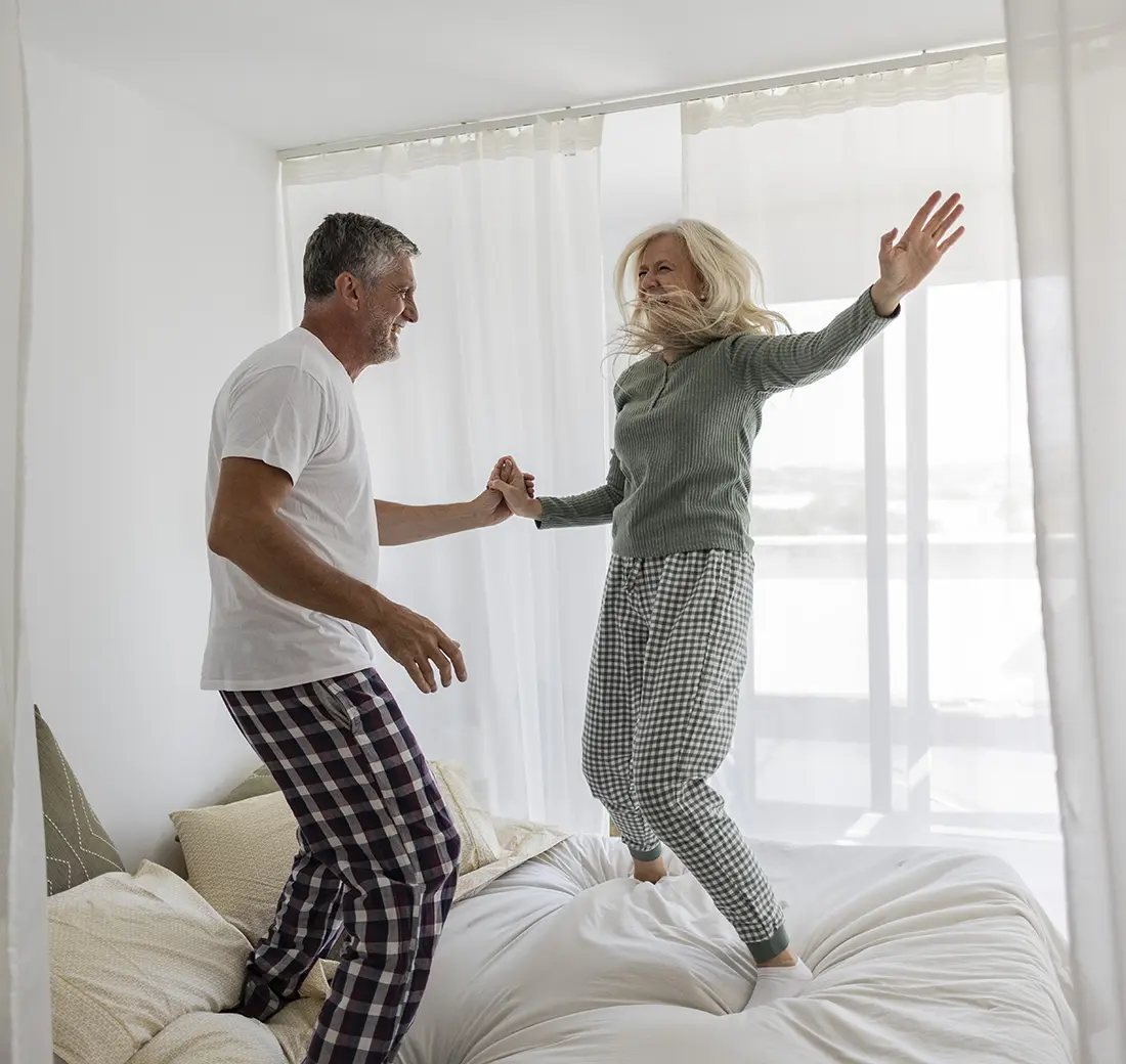 Older couple wearing pajamas jumping on bed