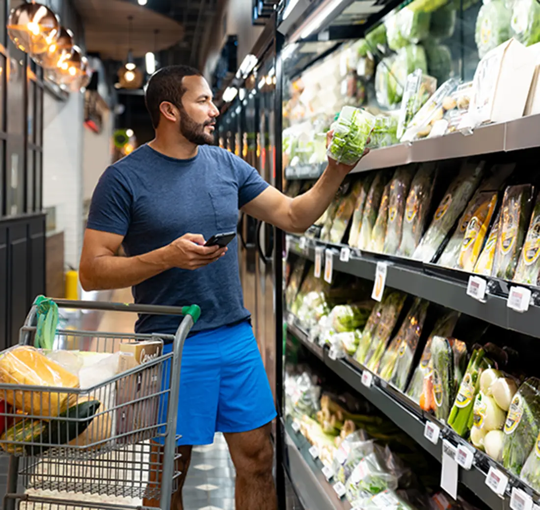 Man looking at container of lettuce at grocery store