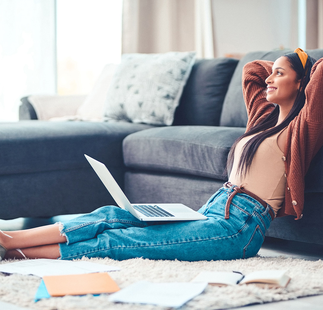 Woman sitting on floor leaning against couch with laptop in her lap