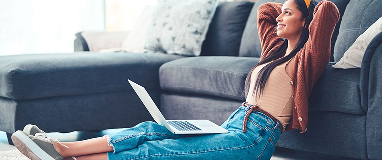 Woman sitting on floor leaning up against a couch with laptop in her lap