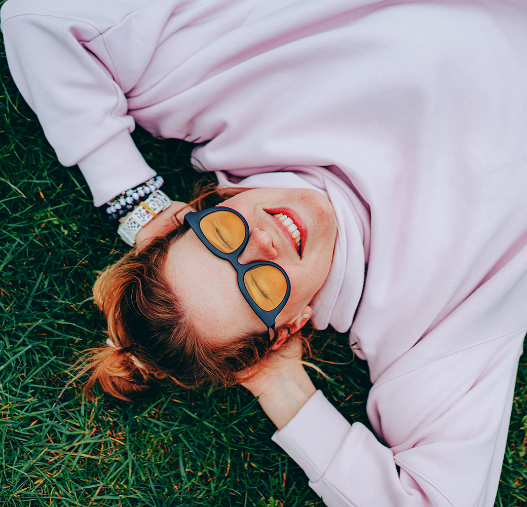 Girl with red hair in a bun laying on grass with hands behind her head