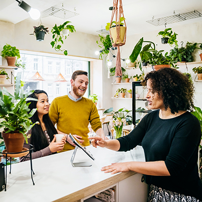A couple ordering their drinks at a café counter surrounded by a variety of plants.