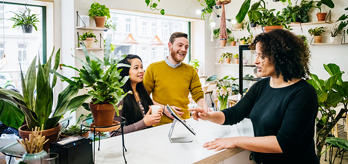 A couple ordering their drinks at a café counter surrounded by a variety of plants.