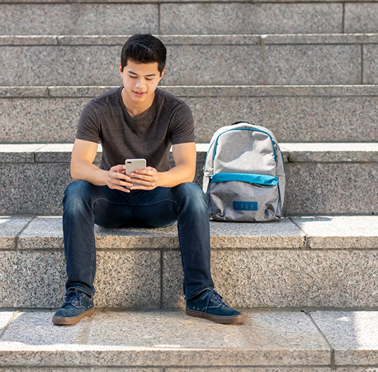 Man sitting on stairs with backpack and typing into his phone