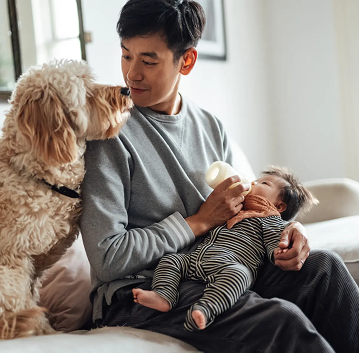 Man feeding baby a bottle while looking at his dog