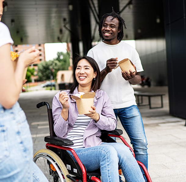 Woman in wheelchair and man behind her holding to go boxes