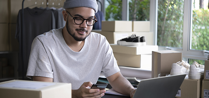 Asian man online seller confirming orders from customer on the phone. E-commerce male business owner looking at the phone in store warehouse.