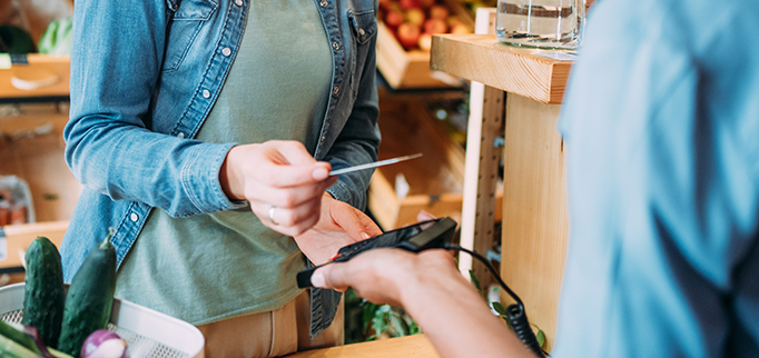 Shot of a female customer making wireless or contactless payment using debit or credit card. Woman paying for groceries at checkout in organic store.